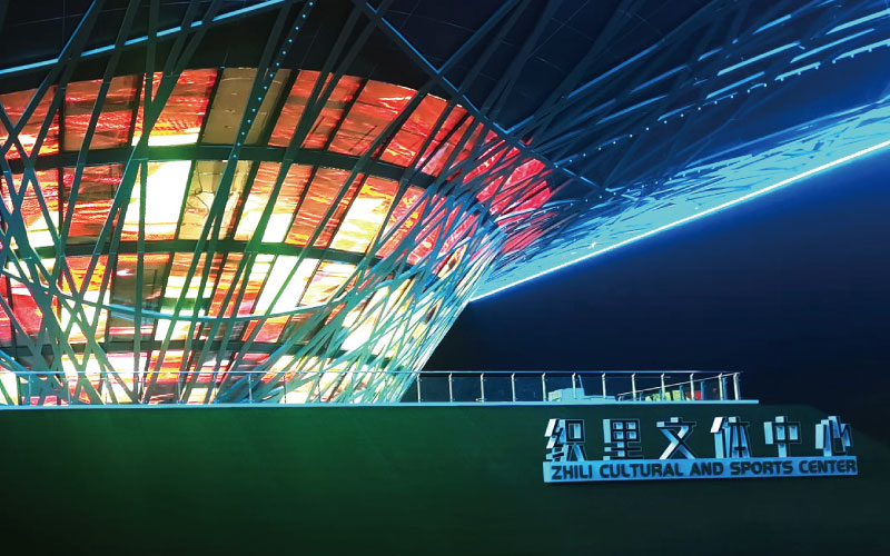 位于浙江湖州的織里文體中心，是一座大型異形鋼架結構建筑。三思為其定制近1000平米透明屏，運用高清LED透明屏及控制系統，將其打造成了一幅巨型建筑媒體立面。